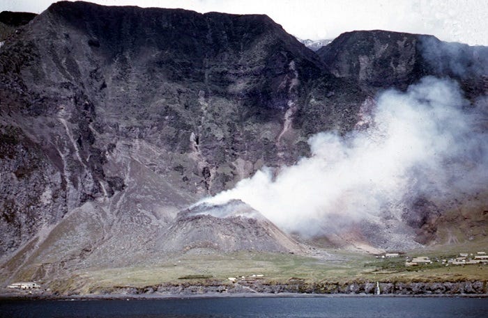 Still from a film shot from HMS Leopard showing the volcano in its early stages behind the settlement Still from a film shot from HMS Leopard showing the volcano in its early stages behind the settlement