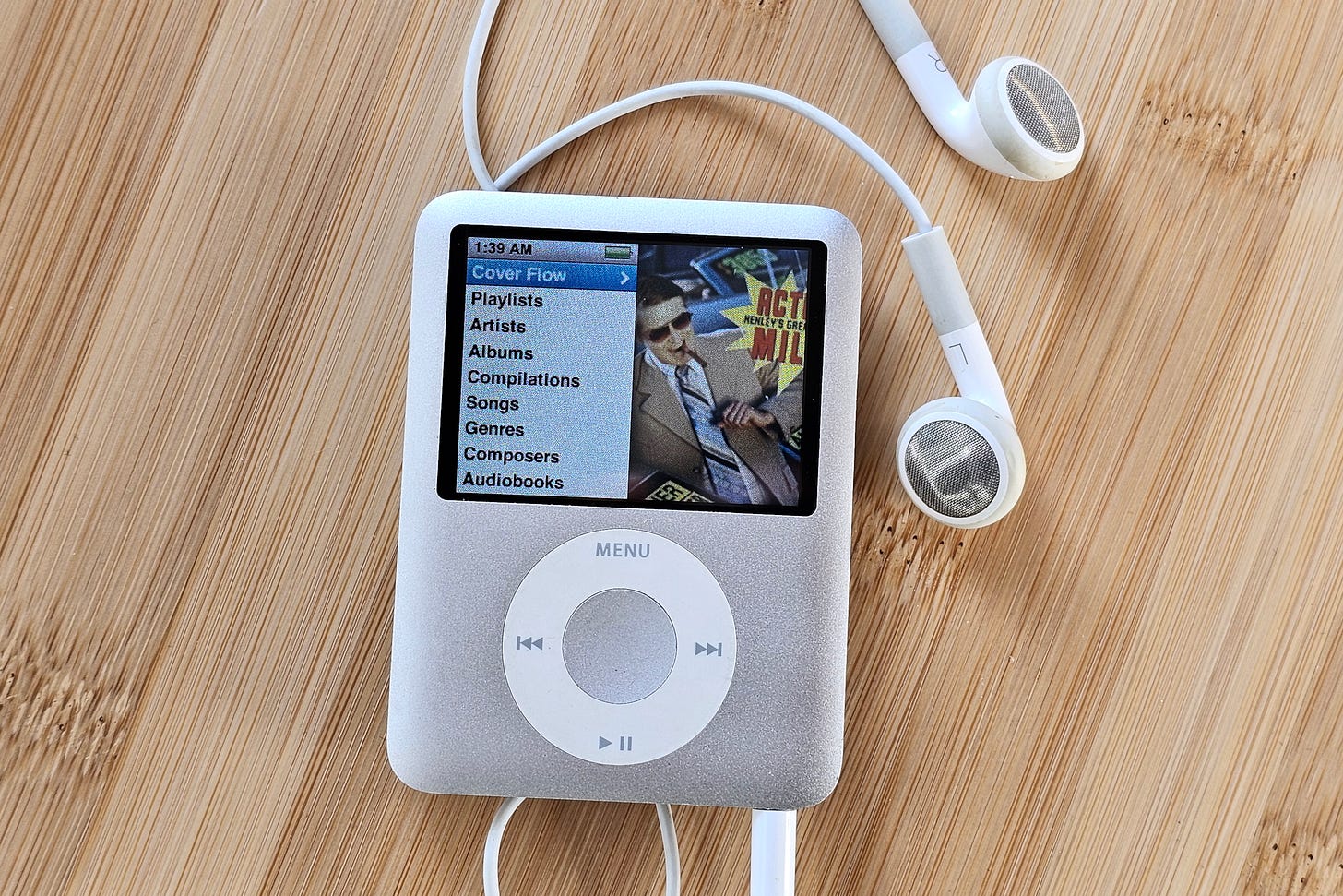 A third-gen iPod Nano in silver with wired earbuds on a bamboo surface. A third-gen iPod Nano in silver with wired earbuds on a bamboo surface.