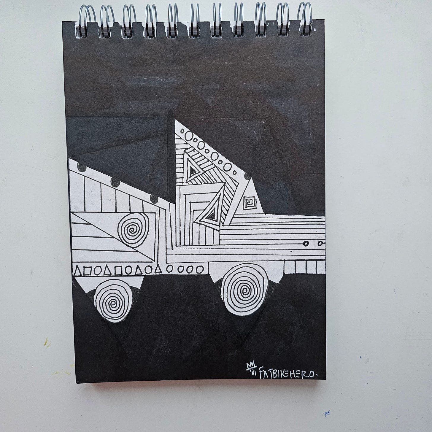 "A horizontal marker drawing by artist FatbikeHero titled Self Driving Firetruck. The artwork is black and white, featuring a stylized, geometric truck made of triangles, rectangles, and lines against a solid black background. The wheels are depicted as spirals. The style is abstract and cubist, resembling a deconstructed blueprint or a toy block construction. Signed 'FatbikeHero' with a crown symbol in the lower right."