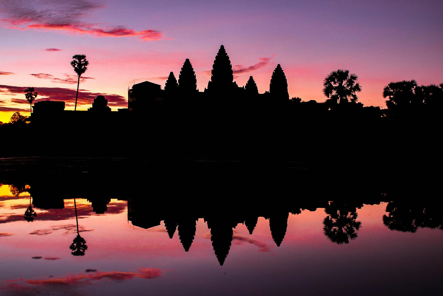 Silhouette of Angkor Wat temple at sunrise, reflected in calm water with pink, purple, and orange hues filling the sky. Iconic Cambodian landmark symbolizing the country’s cultural heritage and a major Southeast Asian tourism destination. Silhouette of Angkor Wat temple at sunrise, reflected in calm water with pink, purple, and orange hues filling the sky. Iconic Cambodian landmark symbolizing the country’s cultural heritage and a major Southeast Asian tourism destination.