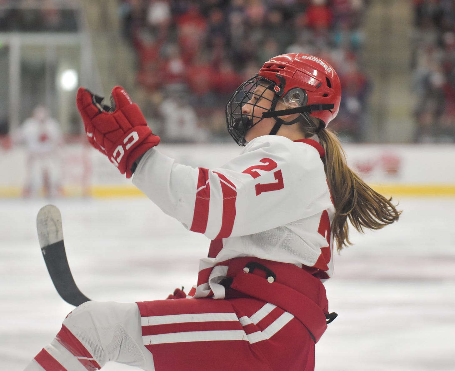 Kirsten Simms skates on one foot with a hand held up in the air