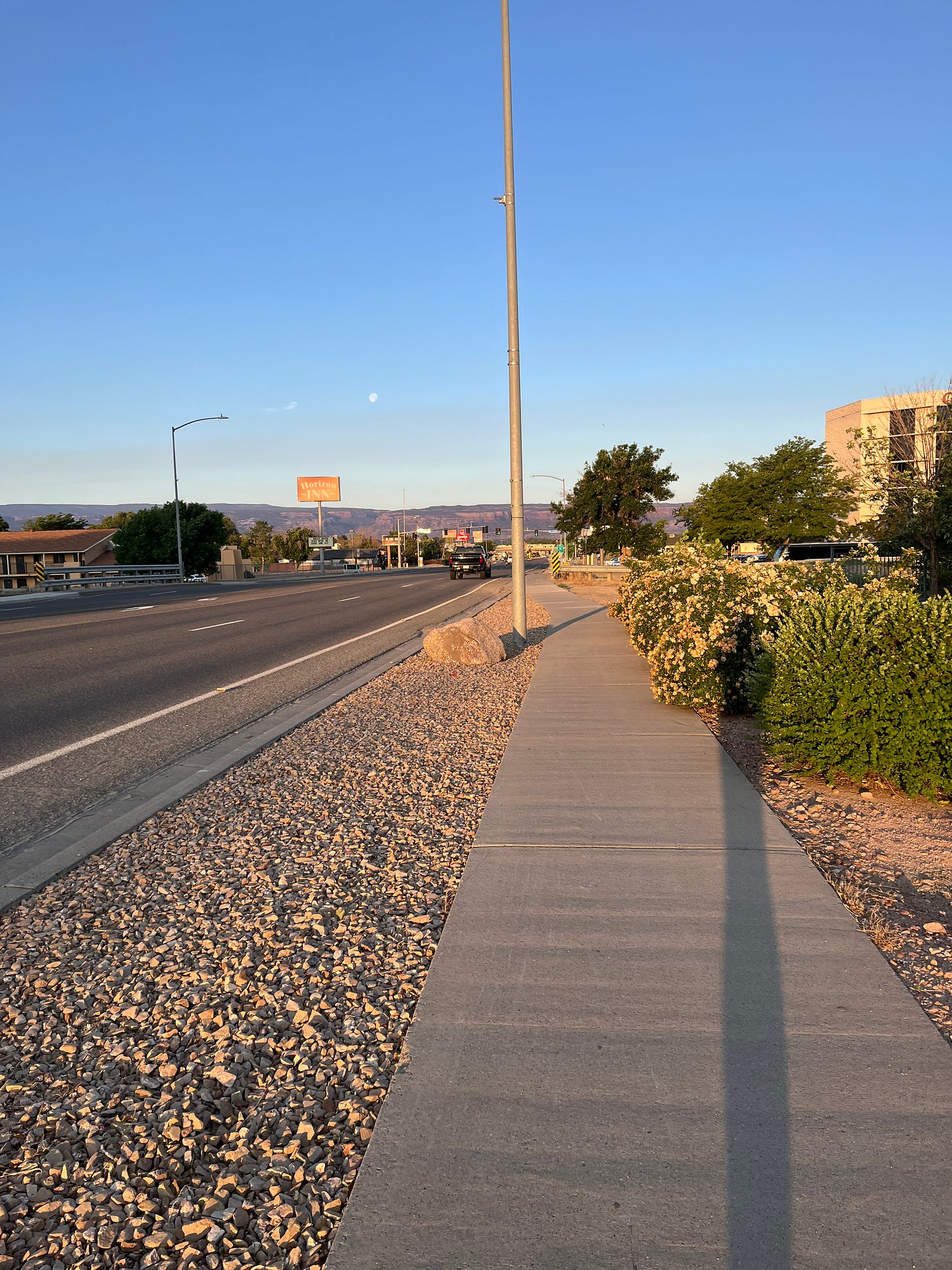 just after sunrise looking at the fullish moon above the mesa beyond a city street lined with hotels