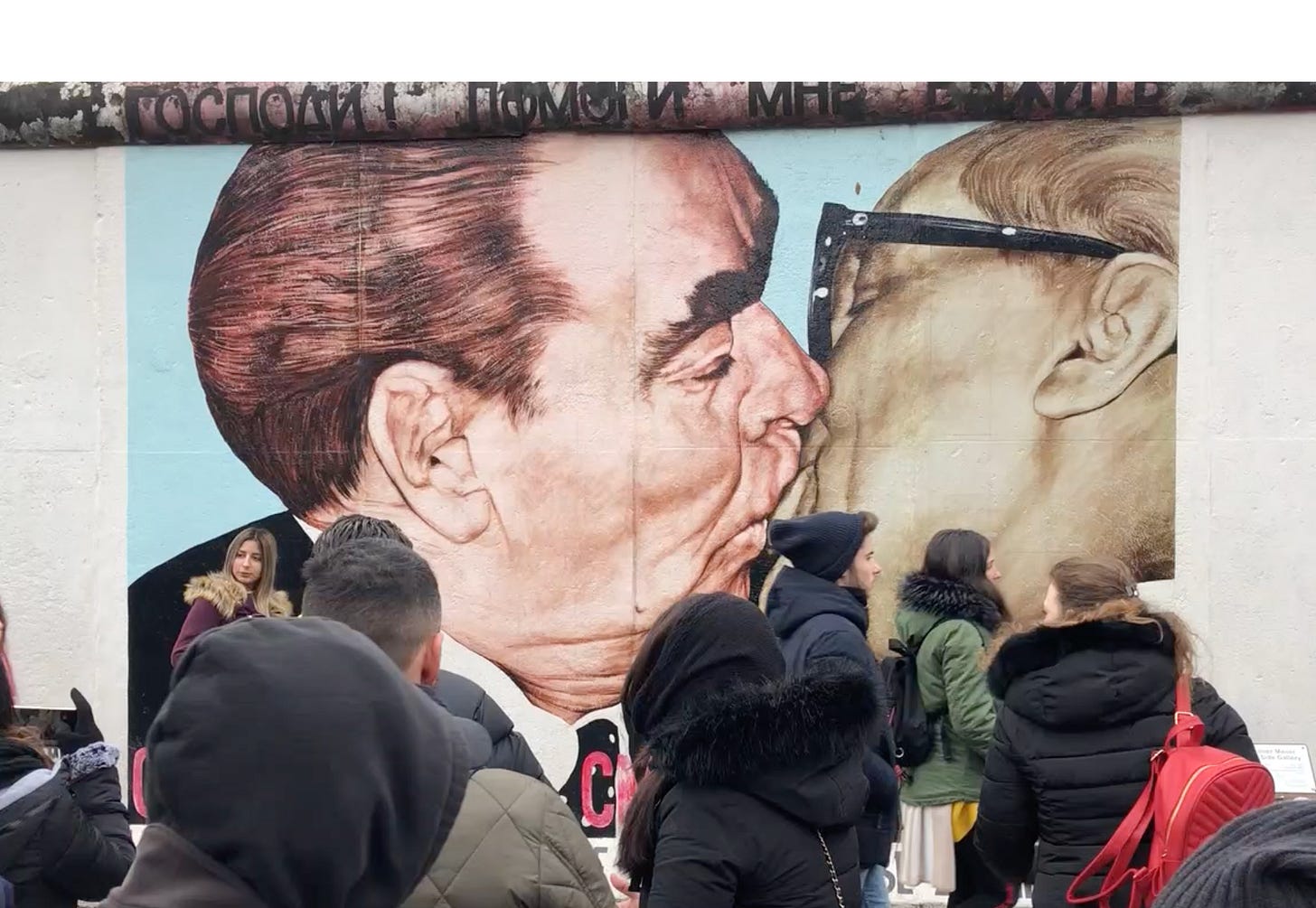 Mural at the East Side Gallery showing Soviet leader Leonid Brezhnev and East German leader Erich Honecker locked in a fraternal kiss, with bystanders viewing the work.