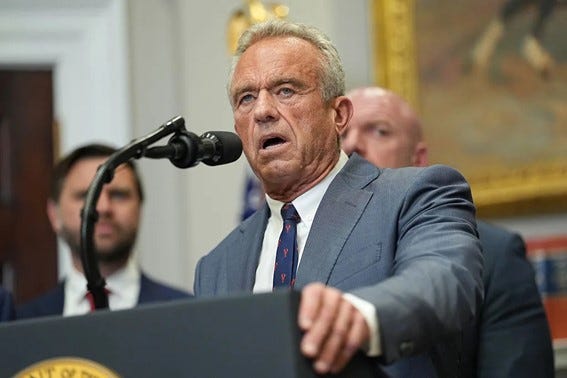 Robert F. Kennedy Jr. (RFK Jr) in a suit and tie speaking passionately at a podium with a microphone, flanked by other individuals in the background.