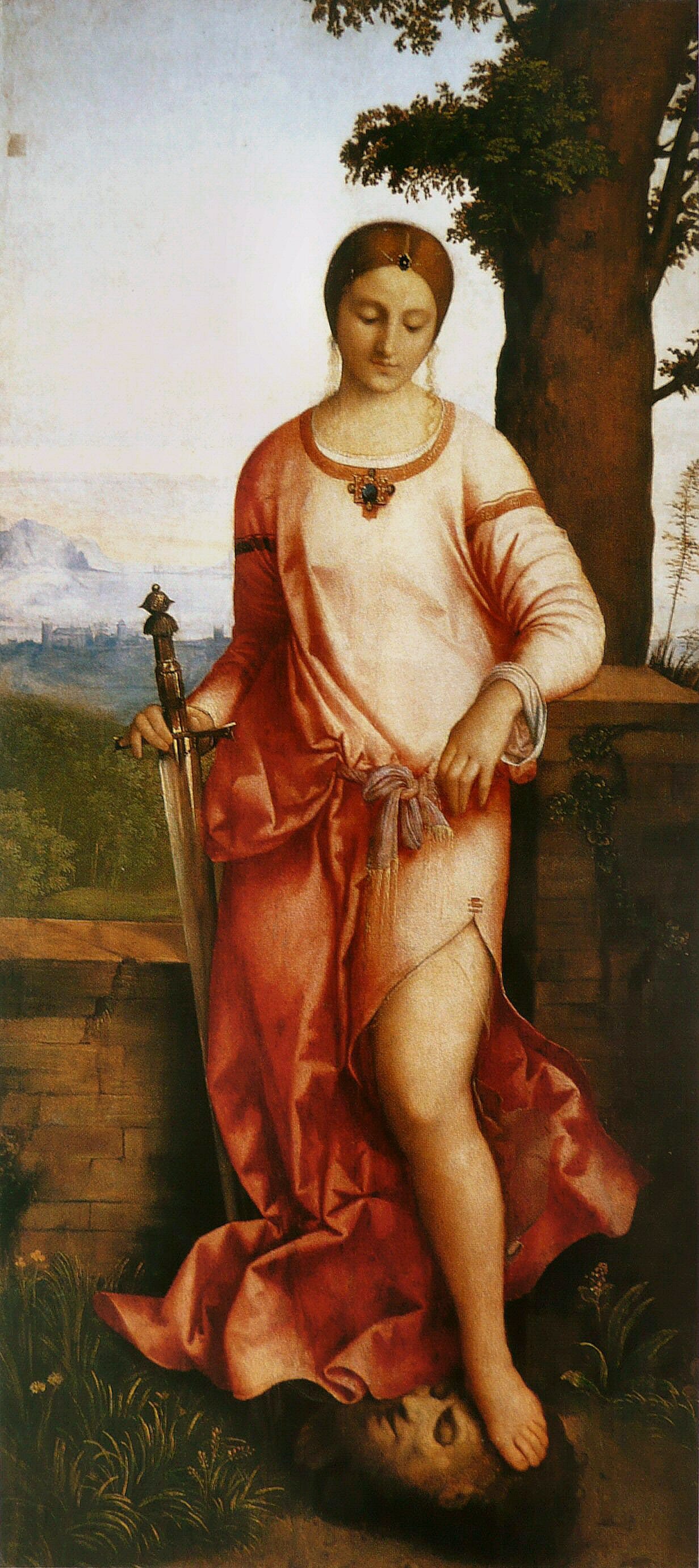 A young woman in a long rose-red dress stands calmly under a tree in a wide green landscape, holding a tall sword point down, her bare foot resting on a man's severed head.