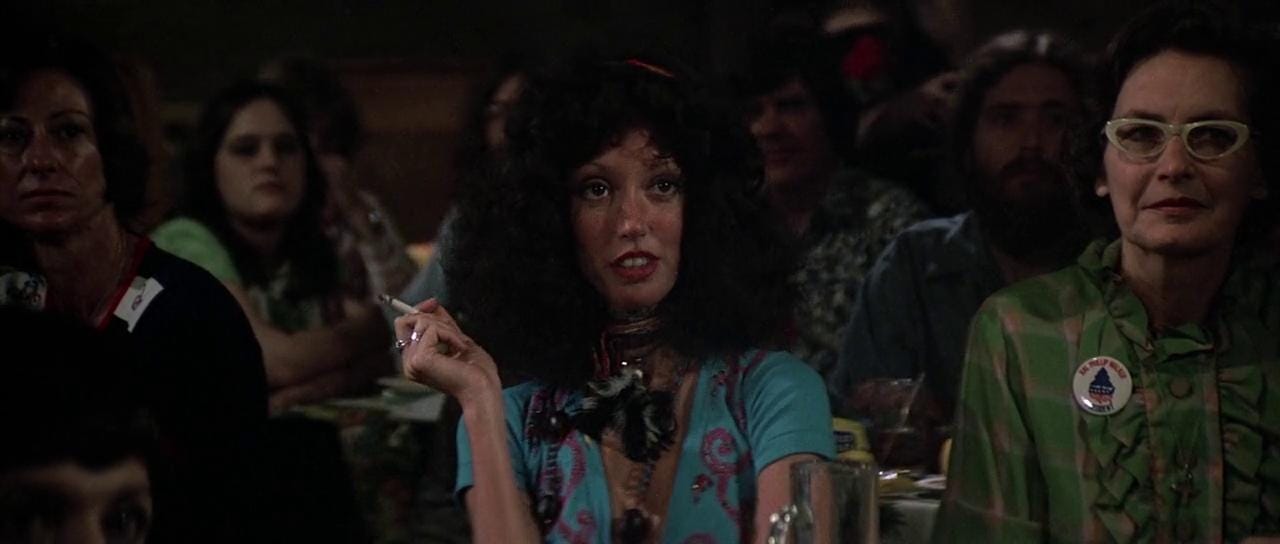 Shelley sits with a crowd, smoking a cigarette