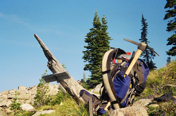 Two men on a mountaintop, a bridge over a creek, a backpack with tools, a waterfall.