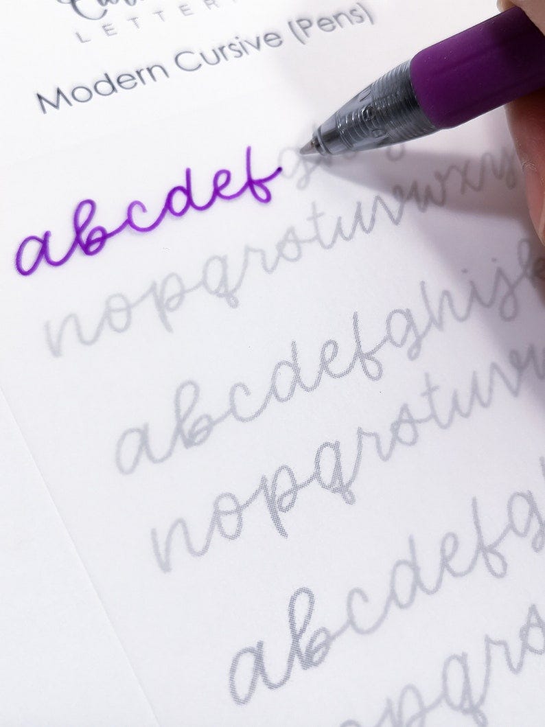 May include: A close-up of a cursive alphabet practice sheet with the letters "abcdef" written in purple ink. The letters "nopqrstuvwxyz" are printed in gray below the purple letters.