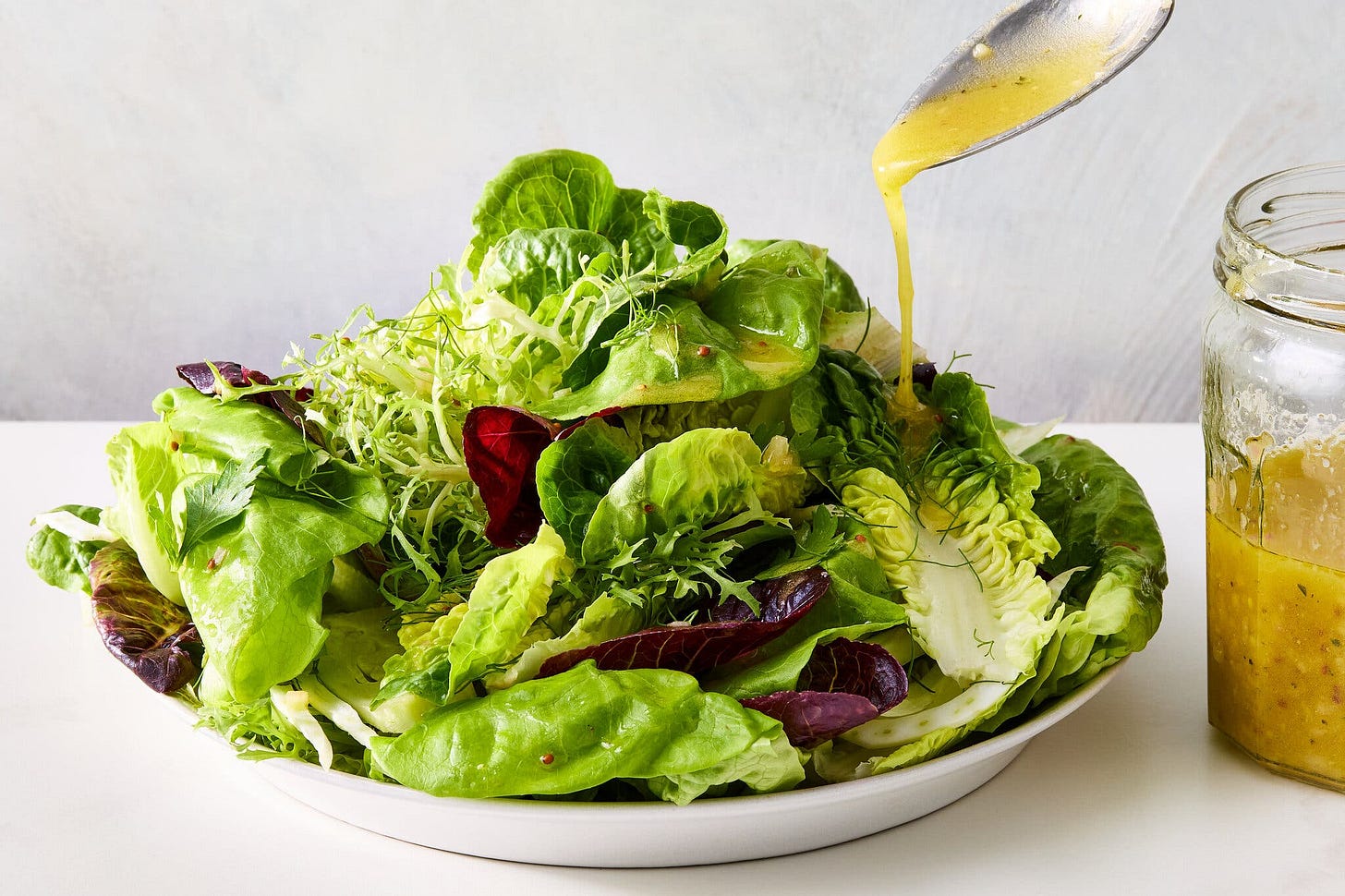 A side image of a tall green salad being drizzled with a golden dressing.