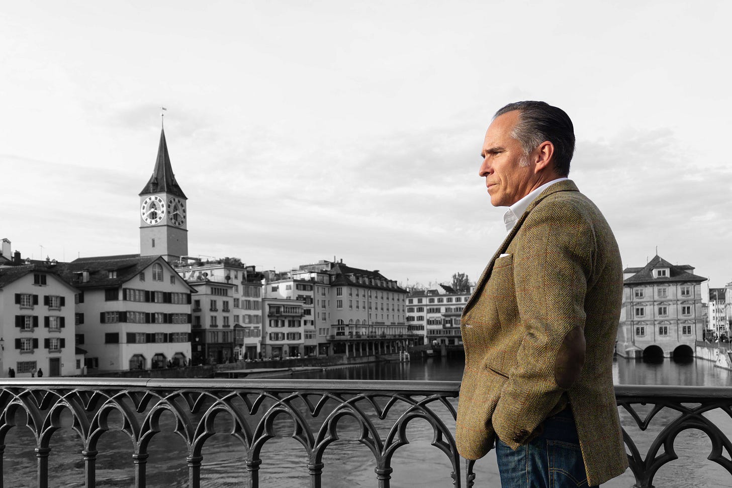 Martin Grassberger steht auf der Münsterbrücke in Zürich und blickt nachdenklich über die Limmat. Im Hintergrund sind die Häuser der Altstadt und der markante Turm der St.-Peter-Kirche zu sehen. Der Hintergrund ist schwarz-weiss gehalten, während Grassberger im Vordergrund farbig hervorgehoben ist. Martin Grassberger steht auf der Münsterbrücke in Zürich und blickt nachdenklich über die Limmat. Im Hintergrund sind die Häuser der Altstadt und der markante Turm der St.-Peter-Kirche zu sehen. Der Hintergrund ist schwarz-weiss gehalten, während Grassberger im Vordergrund farbig hervorgehoben ist.