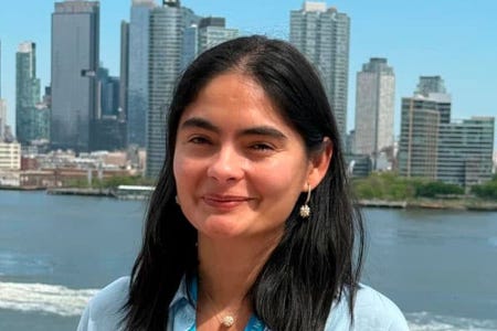 Une jeune feme brune pose en souriant devant le bâtiment new-yorkais de l'ONU