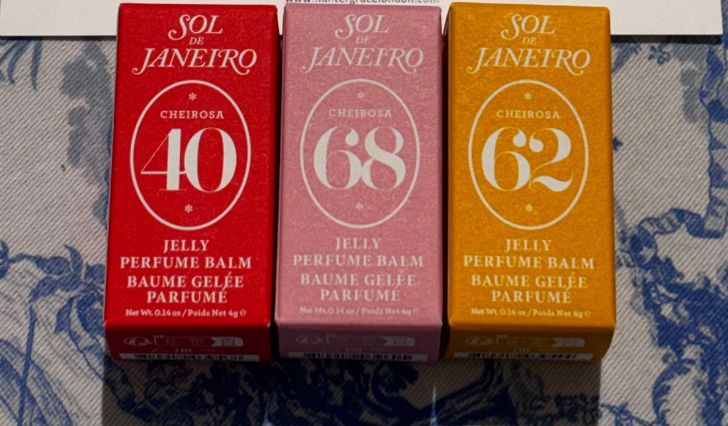 Three closed Sol de Janeiro Jelly Perfume Balm boxes lined up side-by-side on a blue and white patterned textile background. From left to right: a red '40' box, a pink '68' box, and a yellow '62' box. Each box clearly displays the 'Sol de Janeiro' logo and 'Cheirosa' scent number.