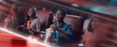 A man eating popcorn in a movie theater is surprised and his popcorn goes flying everywhere.