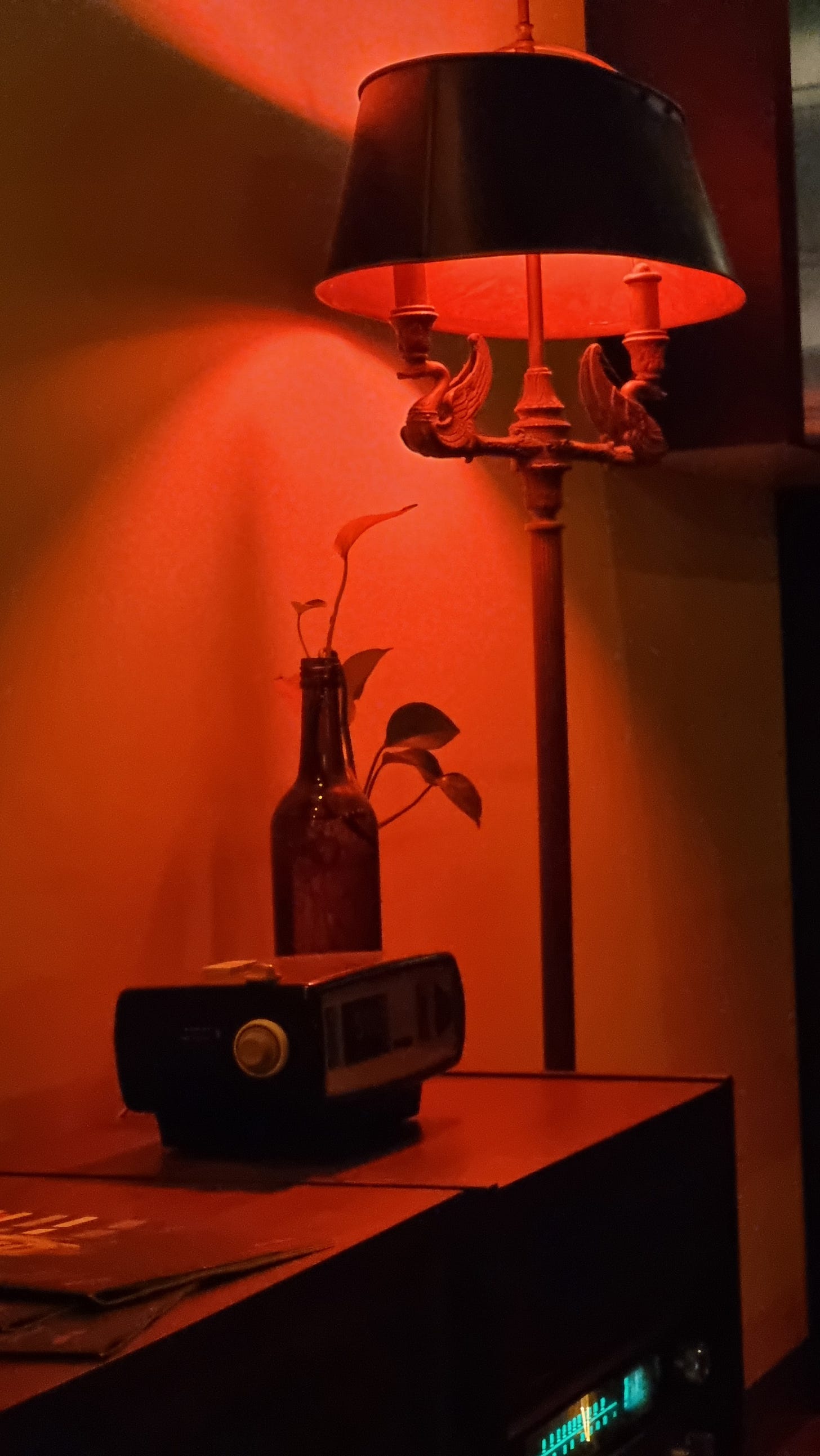 A photo of a lamp casting a reddish glow over an old fashioned radio/speaker and alarm clock. 
