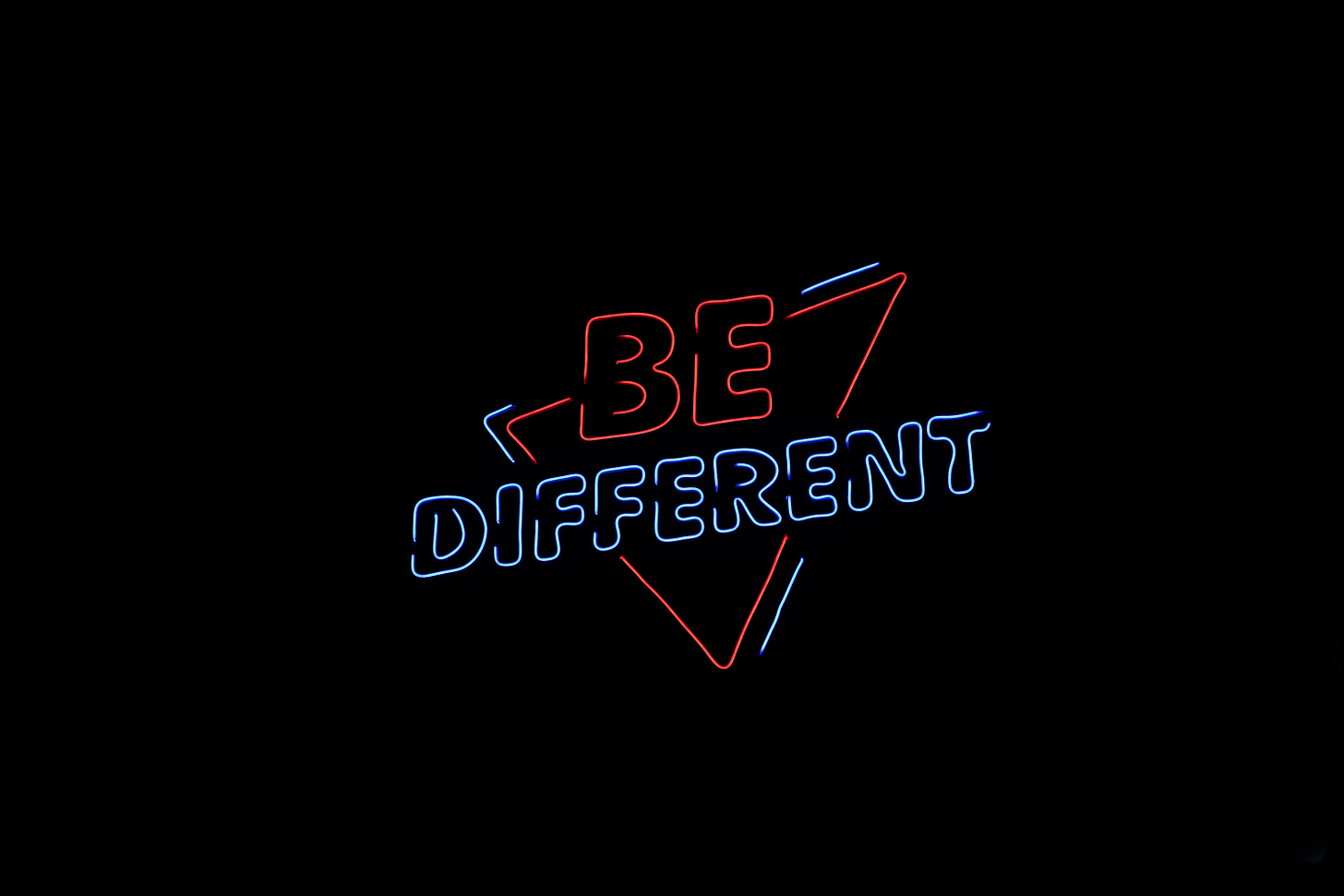 A neon sign with red and blue text that says "be different"