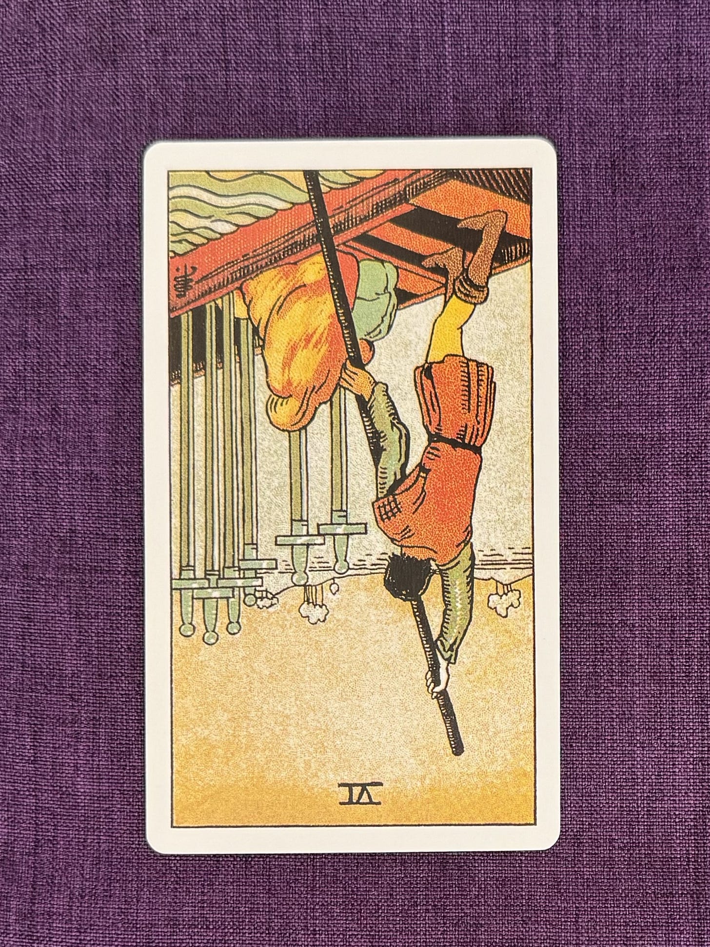 Upside down tarot card shows: The Six of Swords shows a woman and a young child being rowed across a body of water towards a nearby land. Her head is covered, her child nestles in close to her body. In the boat stand six swords.The water on the right of the boat is turbulent, but the sea ahead is tranquil.