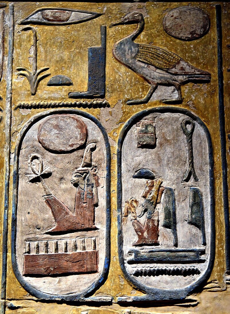 A stone face carved with coloured hieroglyphics. Two cartouches - ovoid shapes with hieroglyphics inside - are visible at the bottom. A stone face carved with coloured hieroglyphics. Two cartouches - ovoid shapes with hieroglyphics inside - are visible at the bottom.