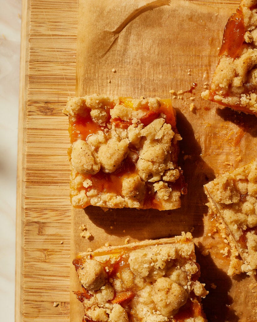 A square of peach bars with brown butter crumble on a wood cutting board A square of peach bars with brown butter crumble on a wood cutting board