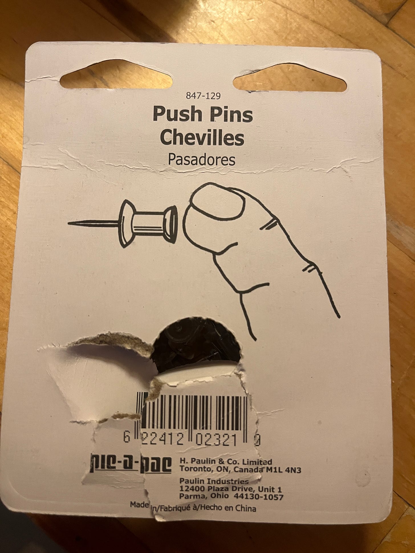 The printed back of a package of push pins with an instructive illustration of how to use the pins. The finger in the illustration is comically oversized and fat, and barely looks like a finger.