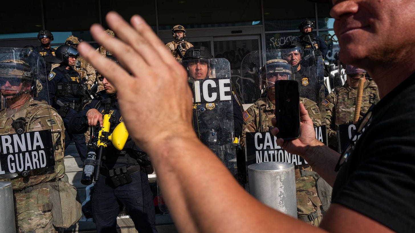 A person holds up their phone in front of the National Guard and police as they confront protesters following three days of clashes with police after a series of immigration raids on June 9, in Los Angeles. A person holds up their phone in front of the National Guard and police as they confront protesters following three days of clashes with police after a series of immigration raids on June 9, in Los Angeles.