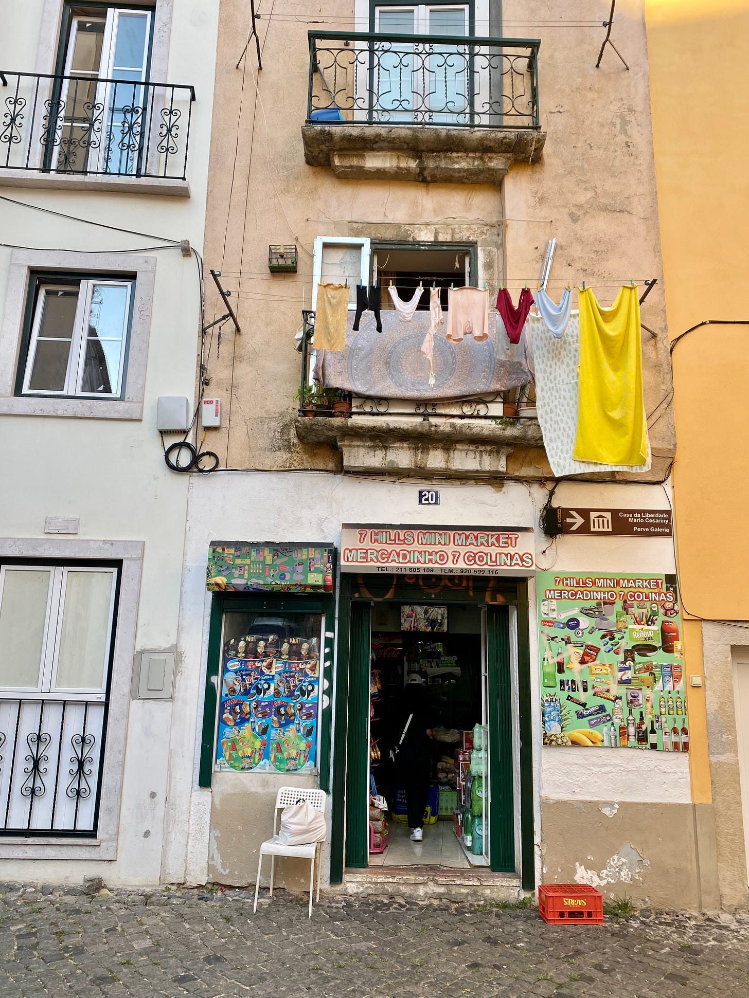 A building in Lisbon with washing hanging from the first floor balcony and a shop door below
