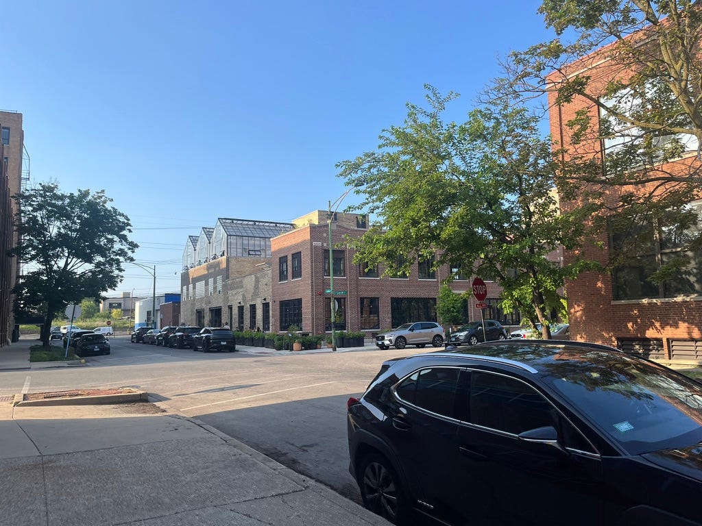 a 2-story brick building beyond an intersection, with a greenhouse visible in the far end of the roof