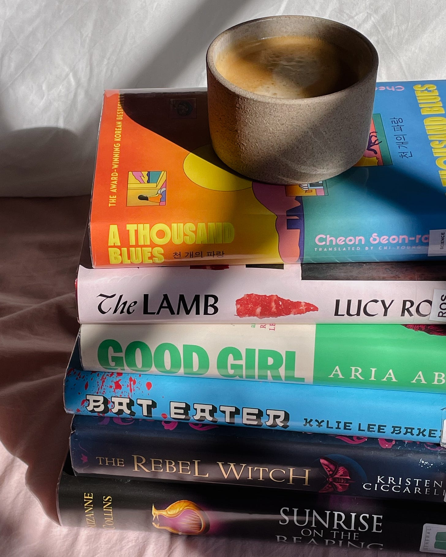 Morning light on my bed, with a stack of read books and a coffee cup resting on top.