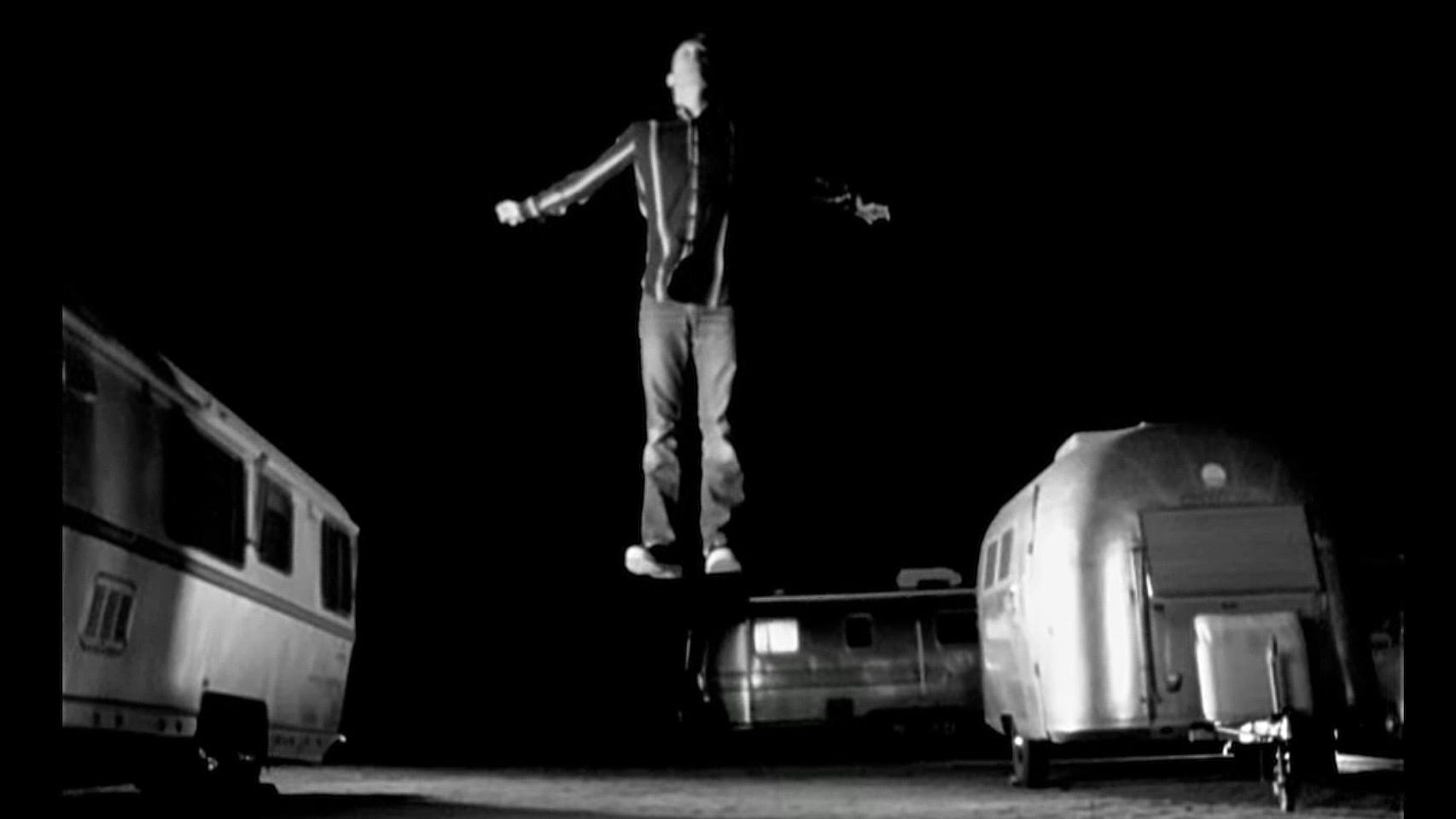 A man hovering a few feet above the ground as if ascending to heaven in a trailer park at night