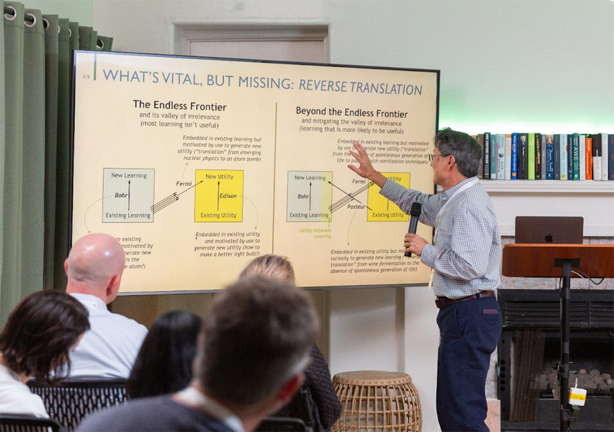 A man gives a presentation, pointing at a slide titled "WHAT'S VITAL, BUT MISSING: REVERSE TRANSLATION," which features diagrams and text explaining learning concepts.