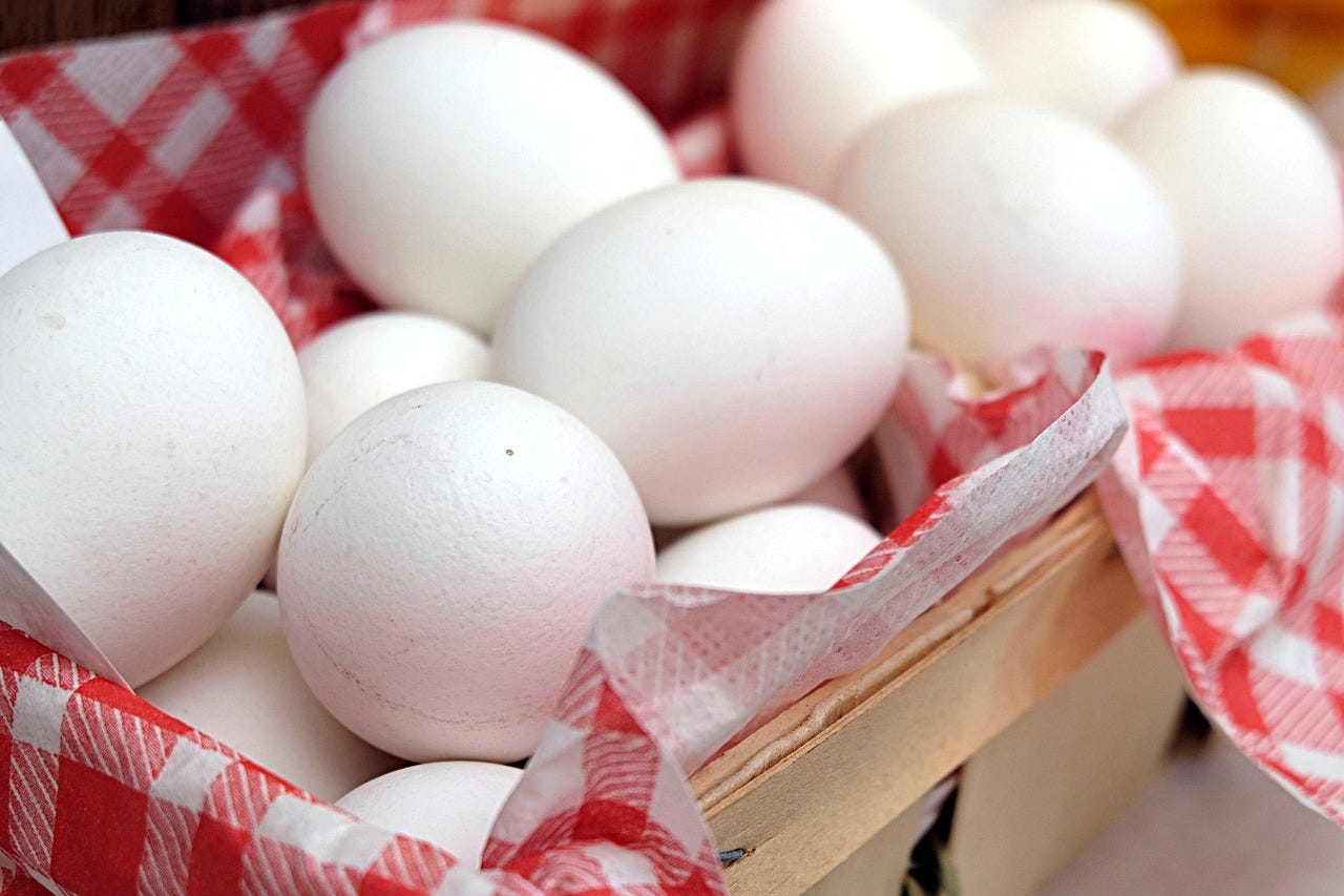 In a basket with a red-and-white checkered cloth are a bunch of white eggs.