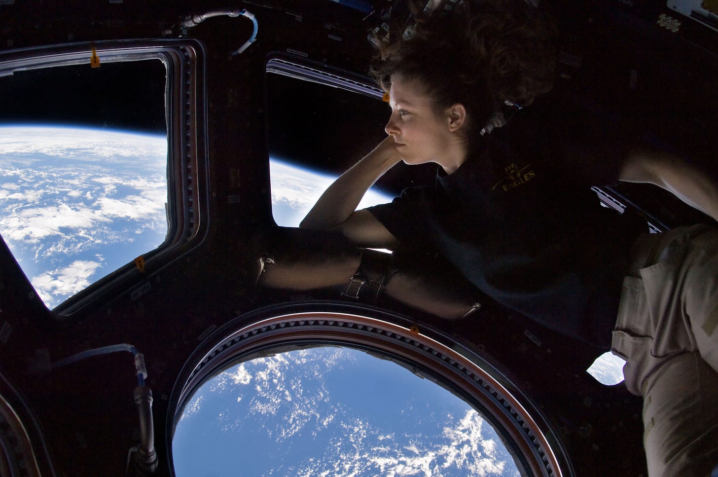 a woman leans against the ISS cupola window, beholding earth below