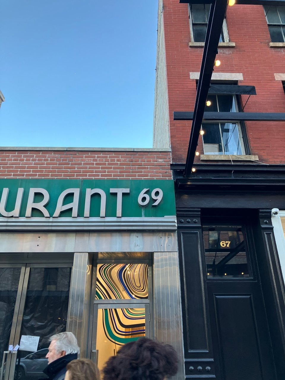Signage showing the end of the word Restaurant and the number 69. silver on green background. the letters have a pleasing swoop and curve to them. 