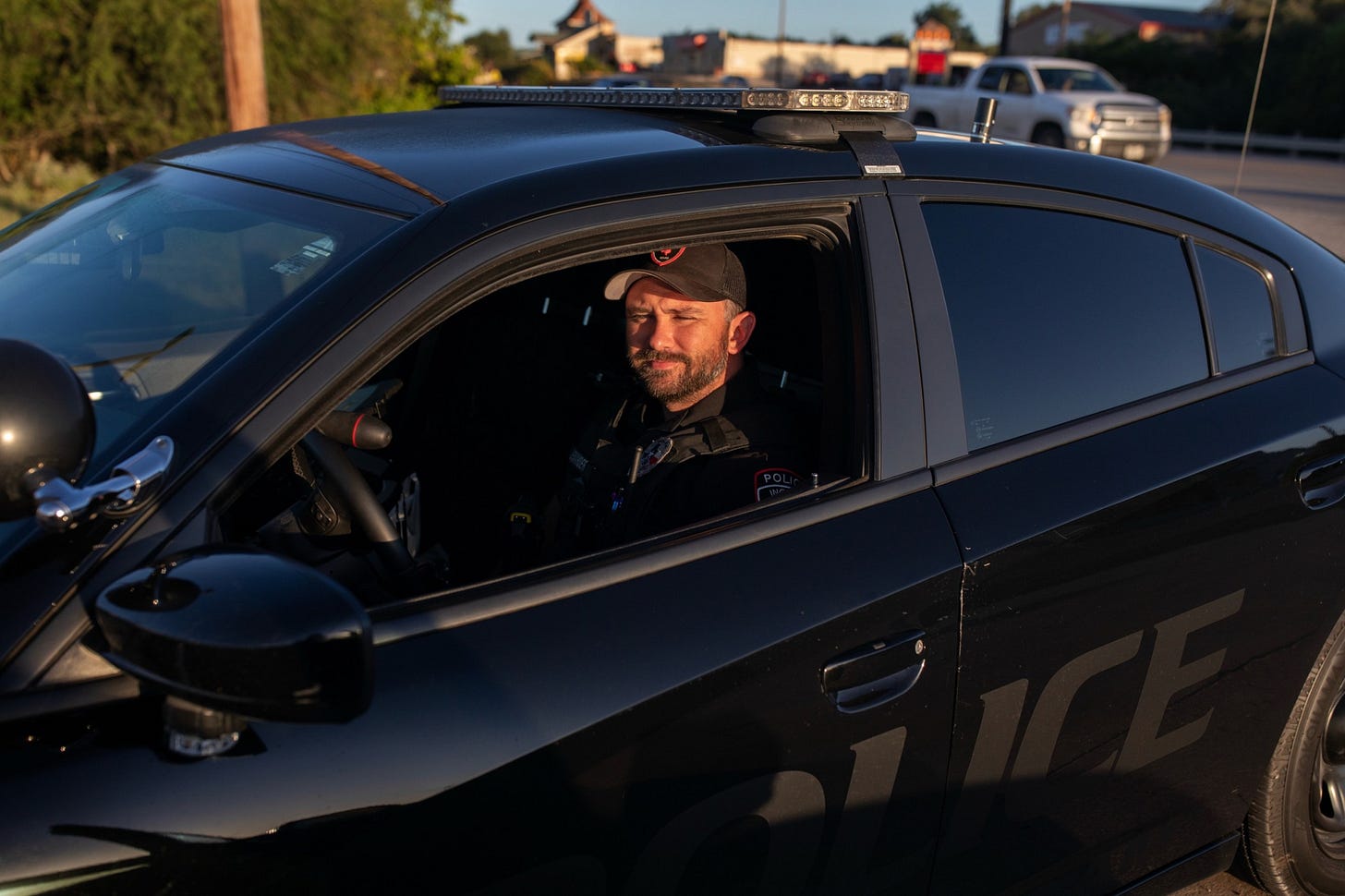 A bearded man wearing a baseball cap and a dark uniform sits in a black Charger. A bearded man wearing a baseball cap and a dark uniform sits in a black Charger.