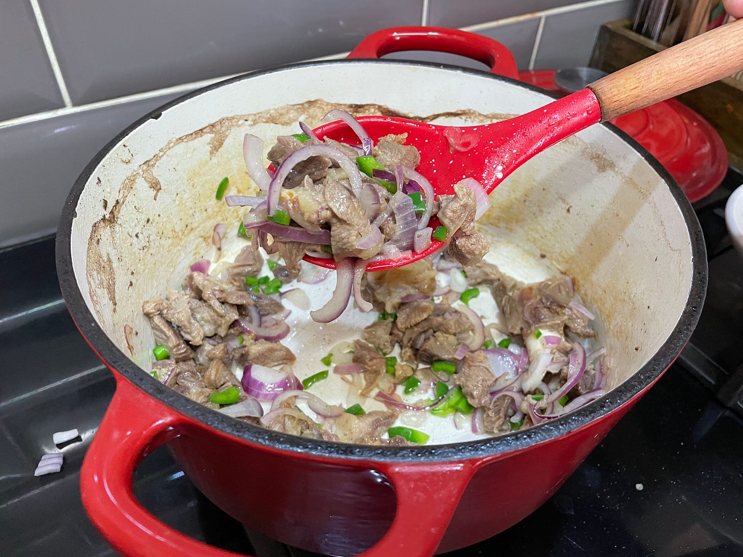 a large pot containing sauteed goat meat and onions and peppers