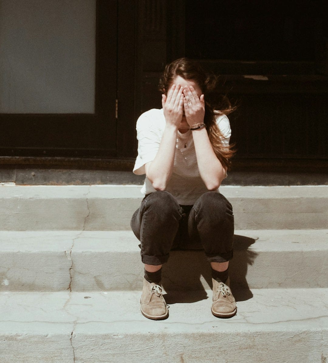 a woman sitting on the steps covering her face a woman sitting on the steps covering her face