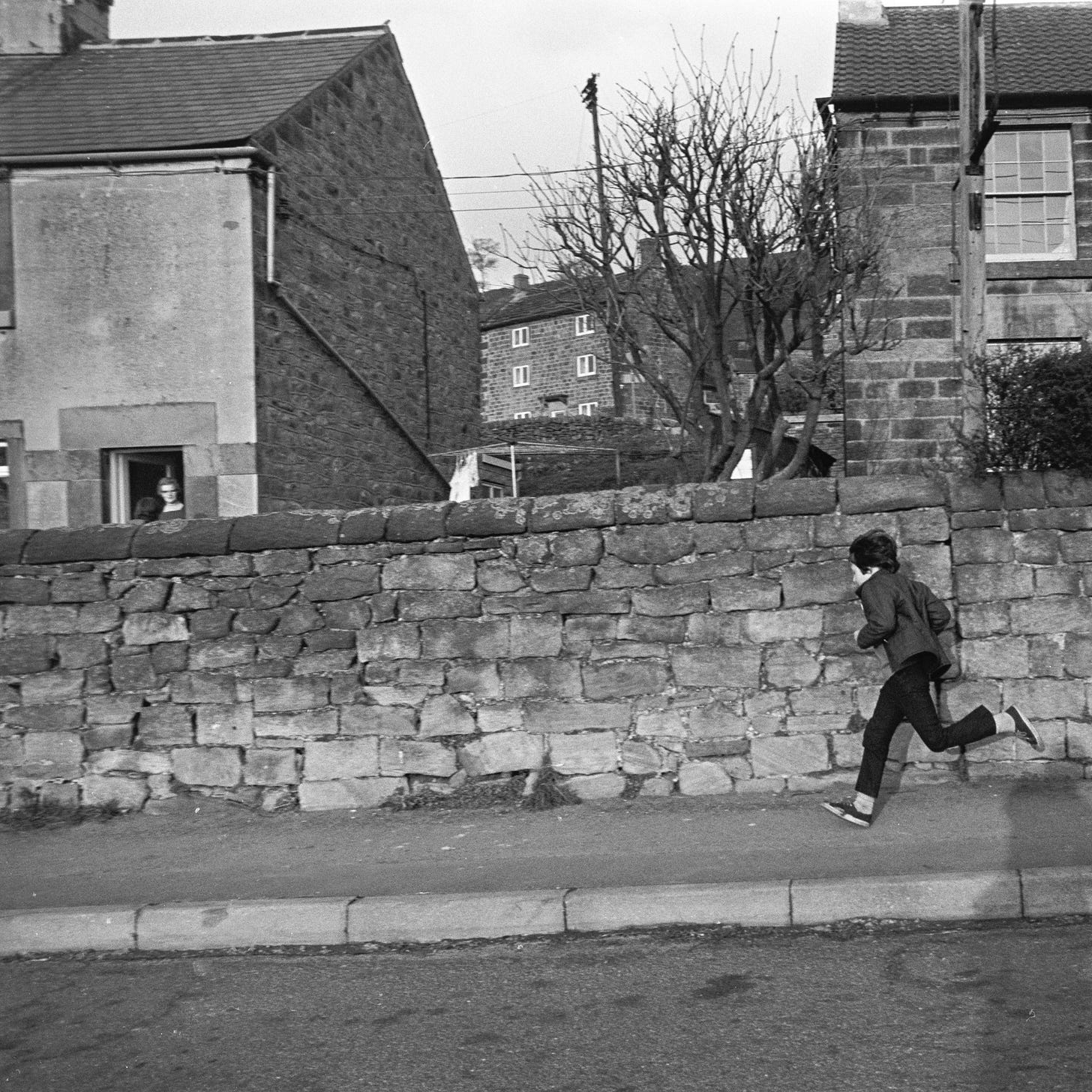 A boy running down the street with a brick fence in front of him, with two houses behind this A boy running down the street with a brick fence in front of him, with two houses behind this