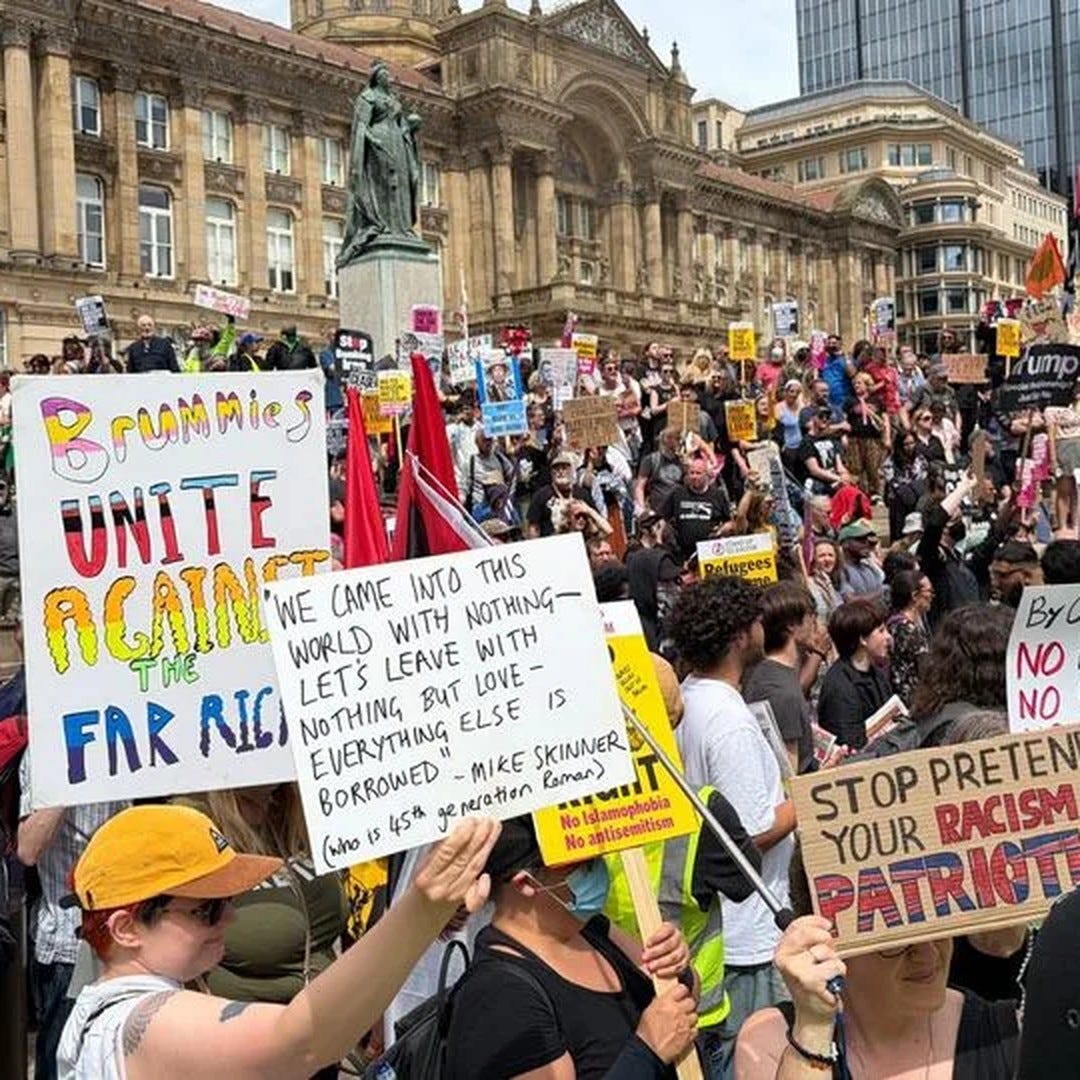 thealmightygob.com-Counter-protesters in Birmingham's Victoria Square holding anti-far-right placards reading "Brummies Unite Against the Far Right" and "Stop Pretending Your Racism Is Patriotism", below the Council House and Queen Victoria statue. thealmightygob.com-Counter-protesters in Birmingham's Victoria Square holding anti-far-right placards reading "Brummies Unite Against the Far Right" and "Stop Pretending Your Racism Is Patriotism", below the Council House and Queen Victoria statue.