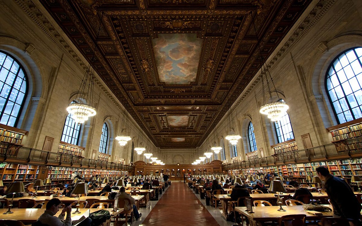Wide interior view of the Rose Main Reading Room at the New York Public Library, featuring long rows of wooden tables, green reading lamps, and an ornate vaulted ceiling painted with murals and architectural detailing.