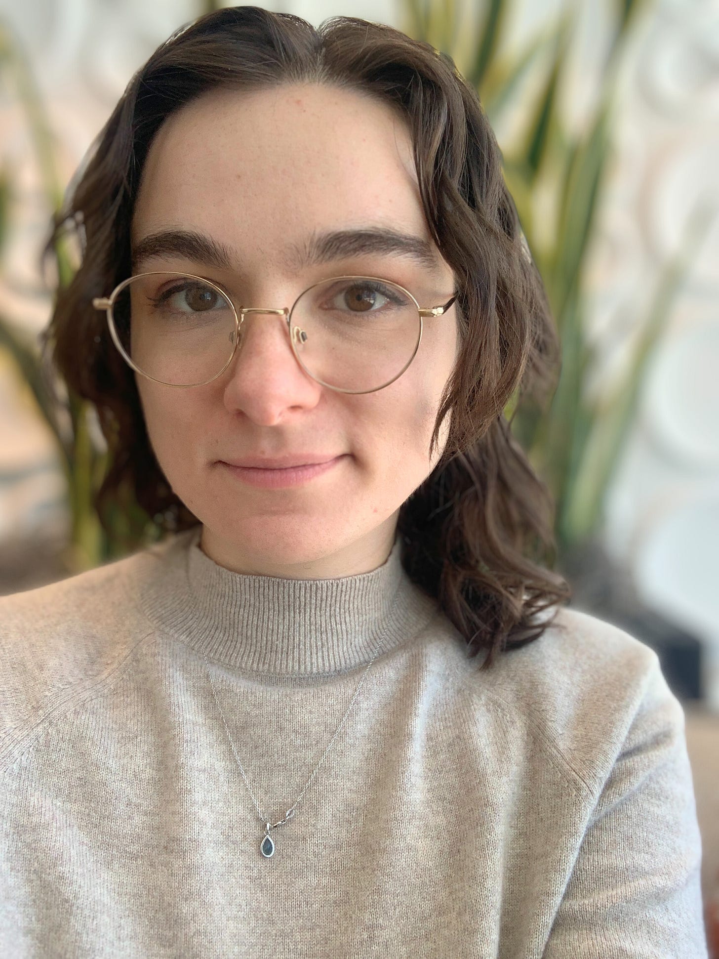 white woman with dark hair and wire rim glasses wearing a beige top