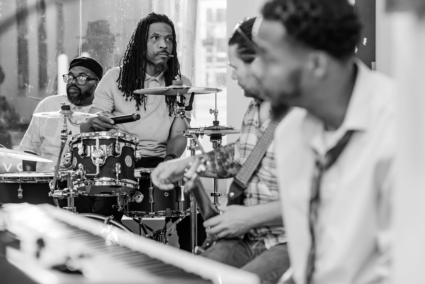 Black-and-white photo of Harvey Road performing at Blondie Mansion Week-End, with drummer in focus and bandmates blurred in foreground. Black-and-white photo of Harvey Road performing at Blondie Mansion Week-End, with drummer in focus and bandmates blurred in foreground.