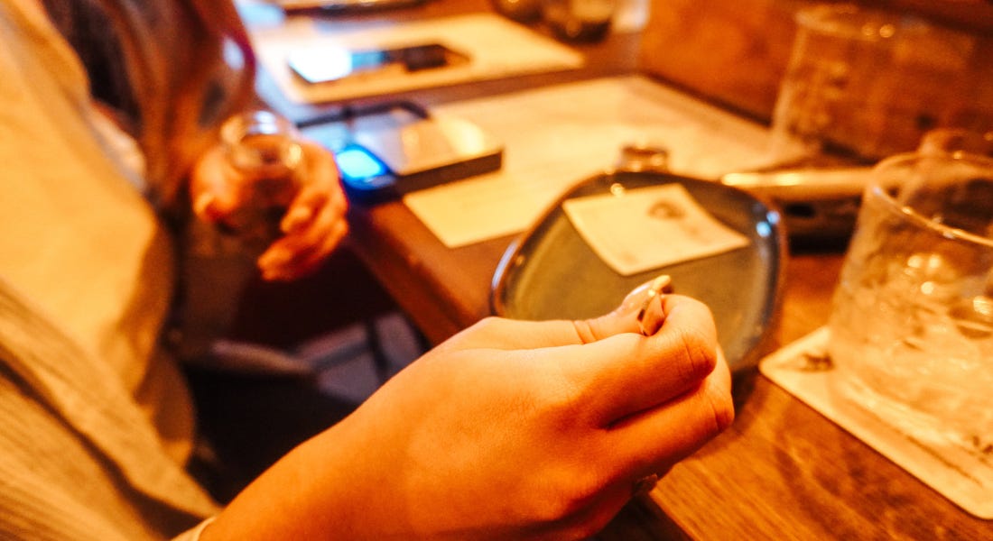 A hand of a woman with long nails using pliers to move ingredients on a plate, with a wooden table beneath A hand of a woman with long nails using pliers to move ingredients on a plate, with a wooden table beneath