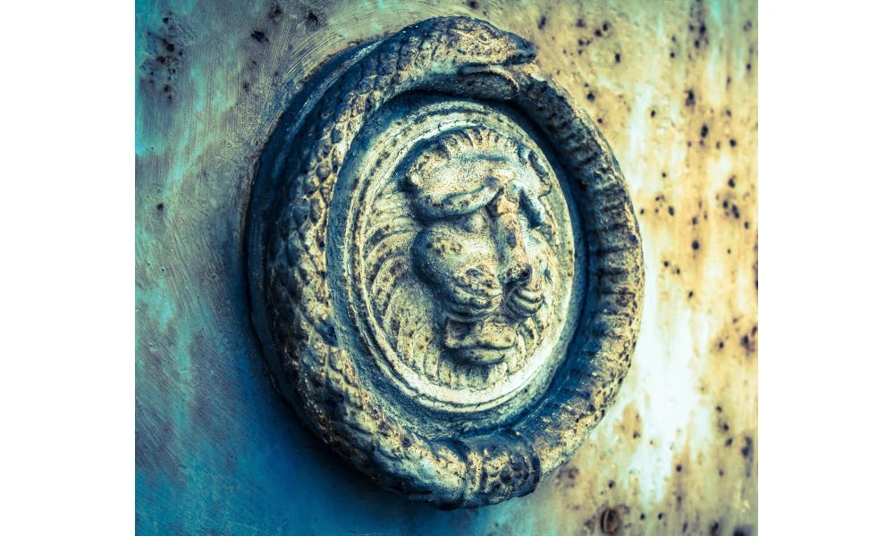 Picture of a snake with its tail in its mouth, the handle on a cemetery door.  The snake is coiled around a leonine face.