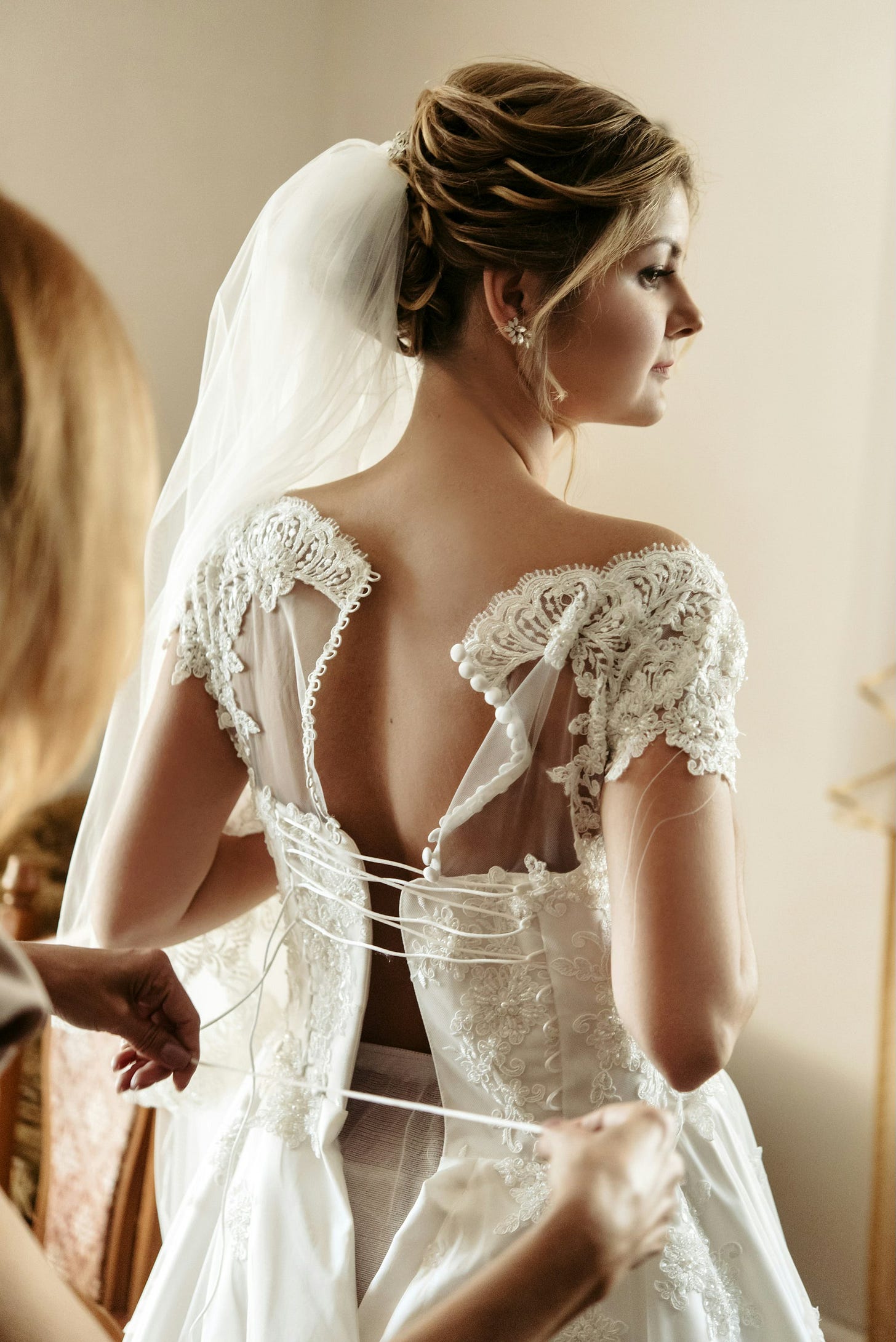a bride having the back of her dress laced up