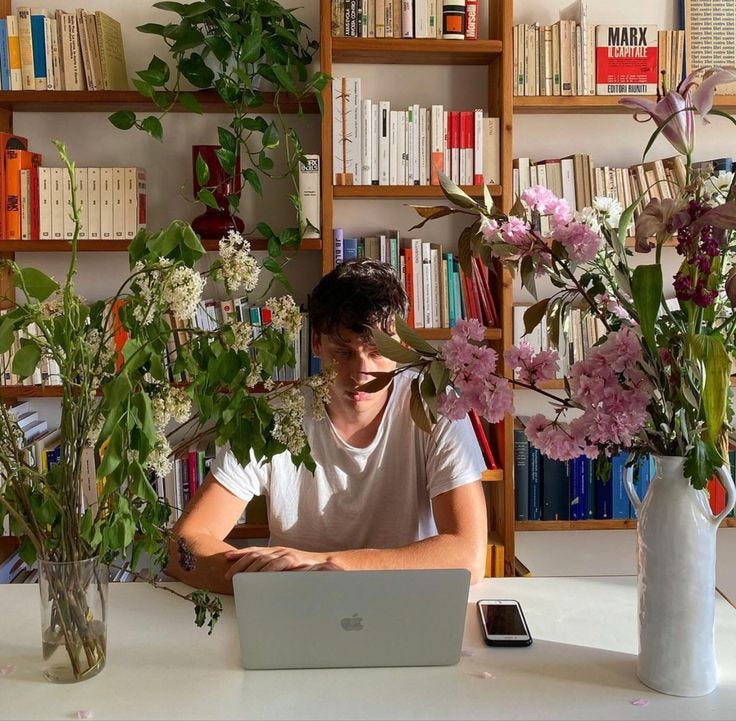 This may contain: a man sitting in front of a laptop computer on top of a table next to flowers This may contain: a man sitting in front of a laptop computer on top of a table next to flowers