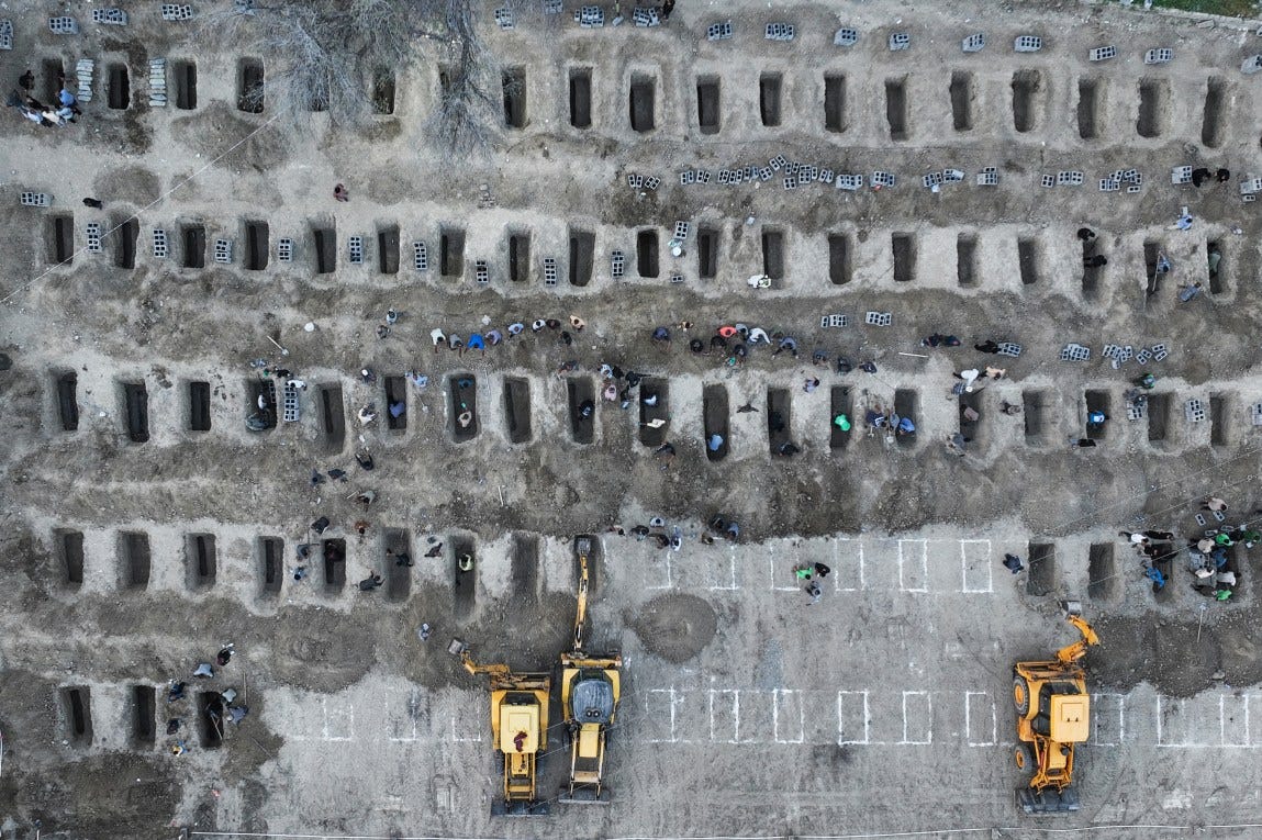 An aerial view of five rows of graves being dug. There are 19 rectangles visible in each row. Earth-moving machines are digging out the holes, and humans with tools are visible all around the site. 