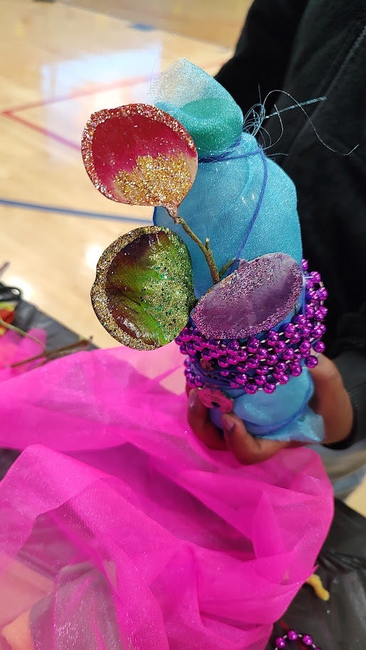 Glittery plastic bottle maraca with seed pods, beads and blue tule.