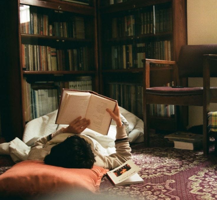 This may contain: a person laying on the floor reading a book in front of a bookshelf