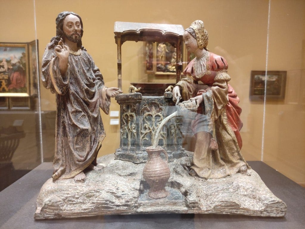 Statue in a display case of Jesus with a Samaritan woman at a well. The woman is looking straight at Jesus while pouring water into an amphora, with the stream going directly in even while she isn't looking. Statue in a display case of Jesus with a Samaritan woman at a well. The woman is looking straight at Jesus while pouring water into an amphora, with the stream going directly in even while she isn't looking.