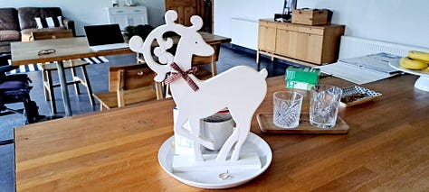 Six photos of stag decorations. 1. cushion with stag head; 2. 2 small black wooden deer ornaments; picture in frame of stag against blue background with message 'Season's Greetings'; white wooden stag figure; two silver stags facing each other with their antlers as candleabra; delicate white ceramic stag tree decoration.