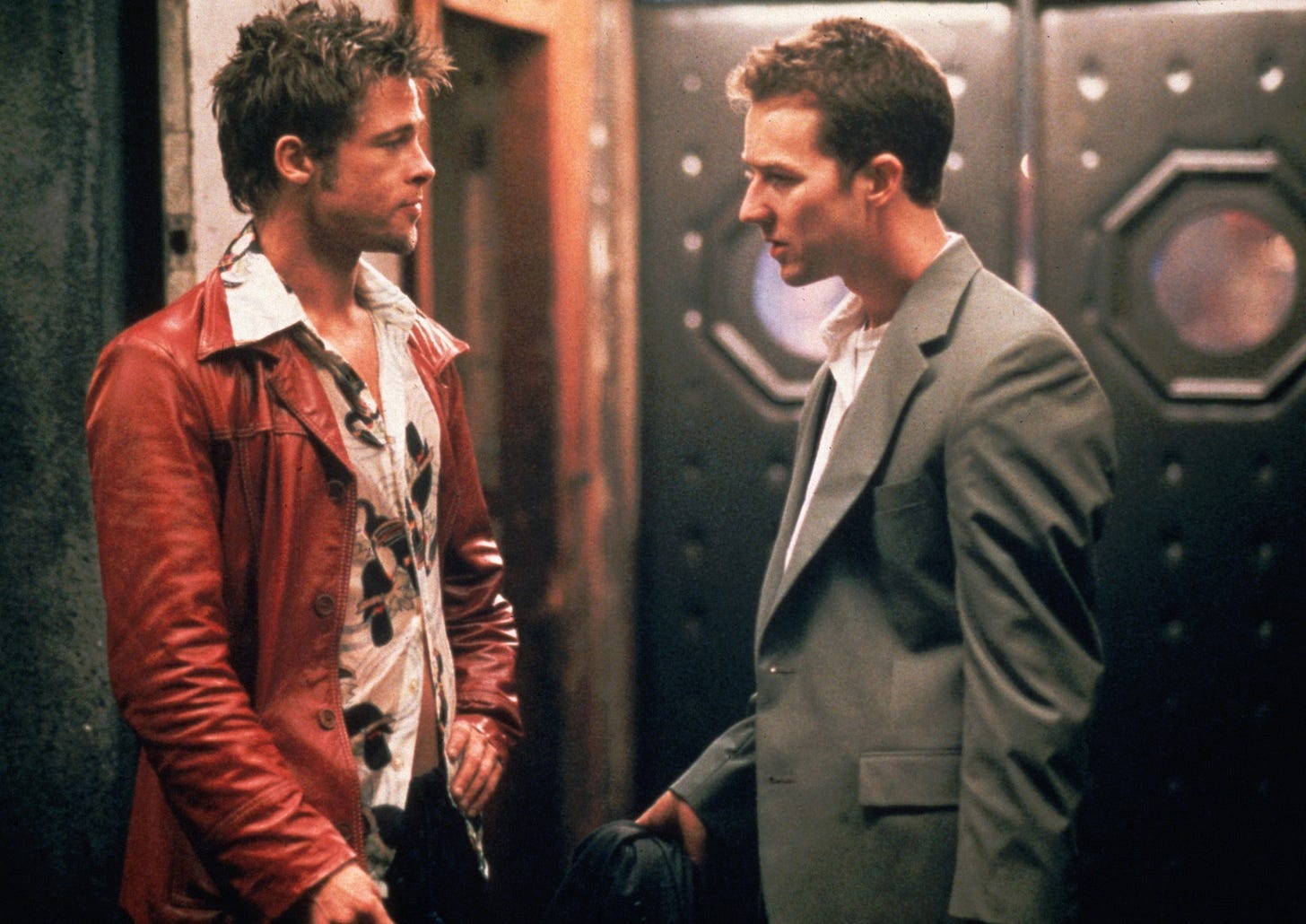 Two men in contrasting outfits having an intense conversation in dimly-lit setting.